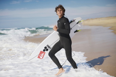 Surfer walking down the beach in a Quiksilver wetsuit with a surfboard
