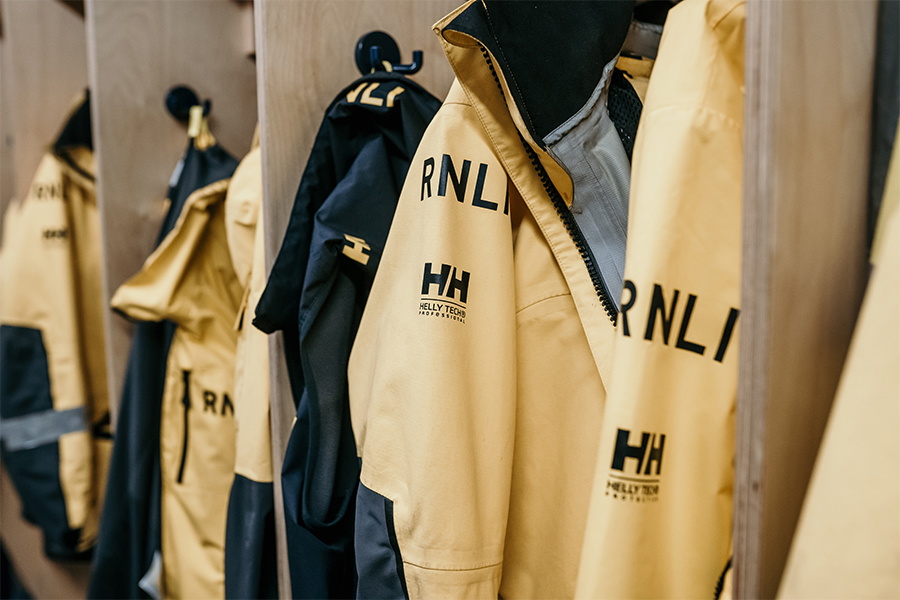 Row of yellow and navy RNLI offshore jackets hanging on hooks in a lifeboat station