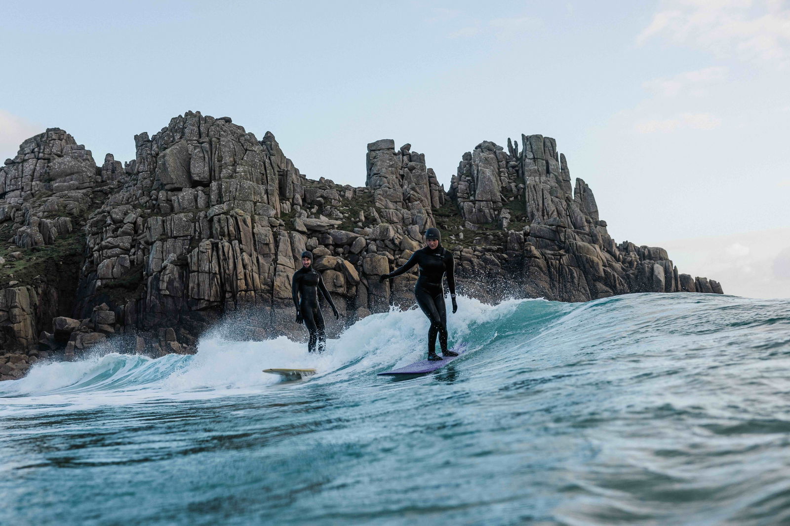 Surfer riding a small clean wave beneath towering granite cliffs