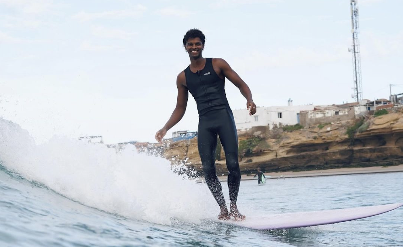 Surfer in a sleeveless black wetsuit riding the whitewater on a longboard