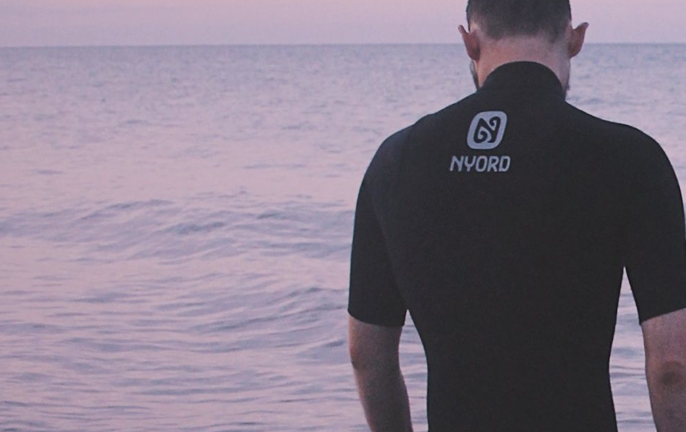 Close-up rear view of a black short-sleeve Nyord wetsuit against a pink dawn sky